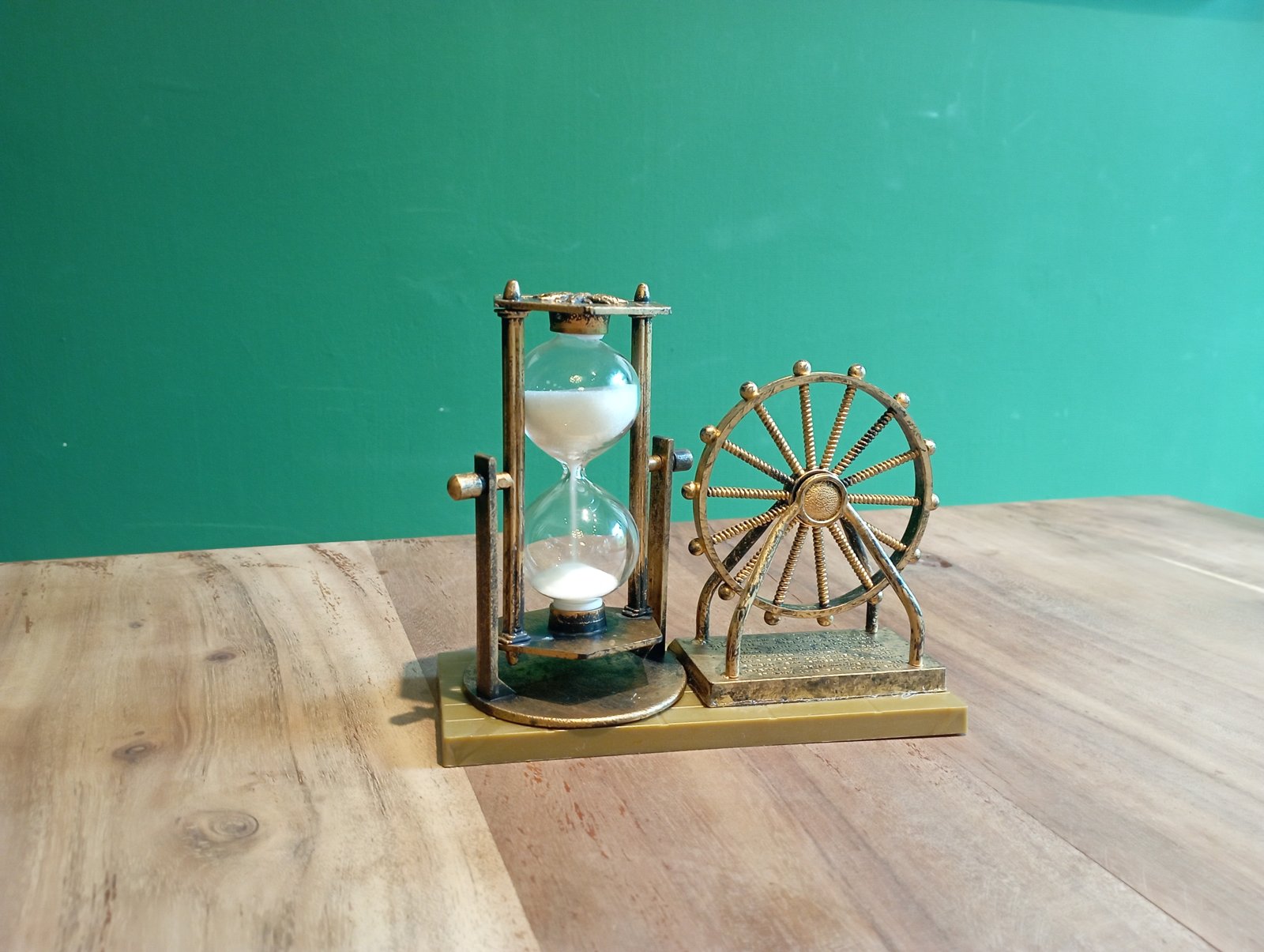 Sanduhr mit weißem Sand auf einem Holztisch vor grüner Wand