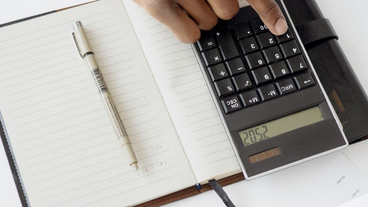 finanzen.net zero Konditionen nachrechnen: Hand am Taschenrechner neben Notizbuch