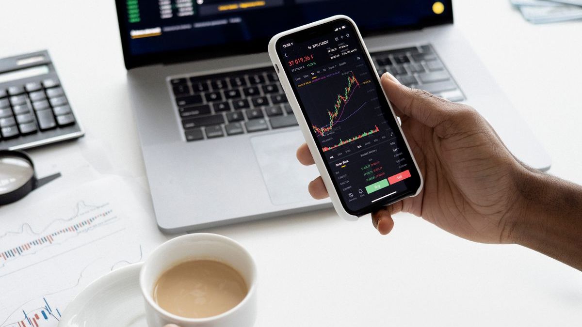 Scalable Capital Konditionen: Hand hält Smartphone mit Kurschart vor Laptop